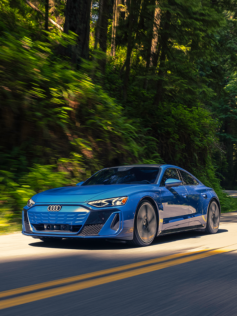 Blue Audi e-tron GT driving on a winding forest road, showcasing electric performance and luxury design.