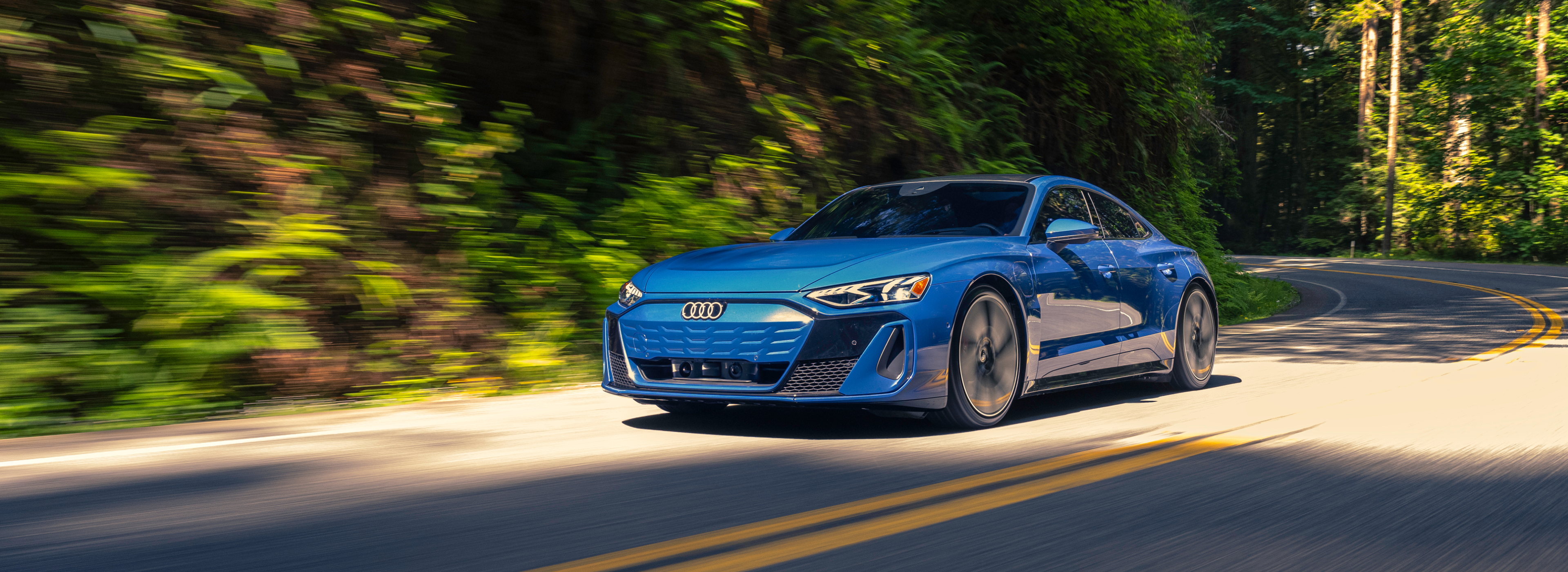 Blue Audi e-tron GT driving on a winding forest road, showcasing electric performance and luxury design.