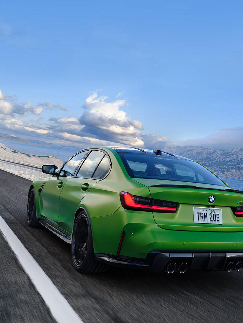 BMW M3 sports sedan driving along a coastal mountain road, showcasing its green exterior, performance design, and dynamic handling.