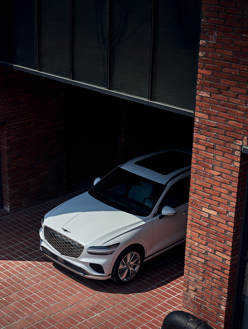 White Genesis GV70 SUV parked in a brick courtyard between two buildings.