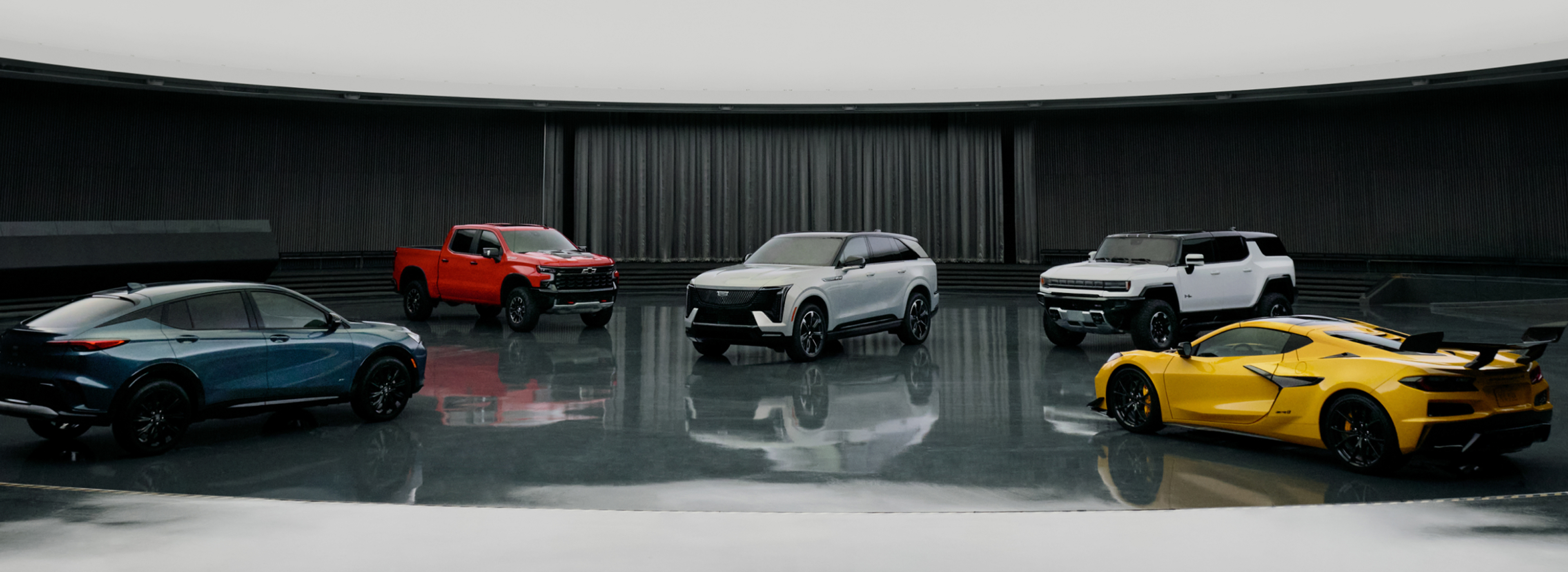 Lineup of GM cars, SUVs, and a truck showcased in a sleek indoor studio.