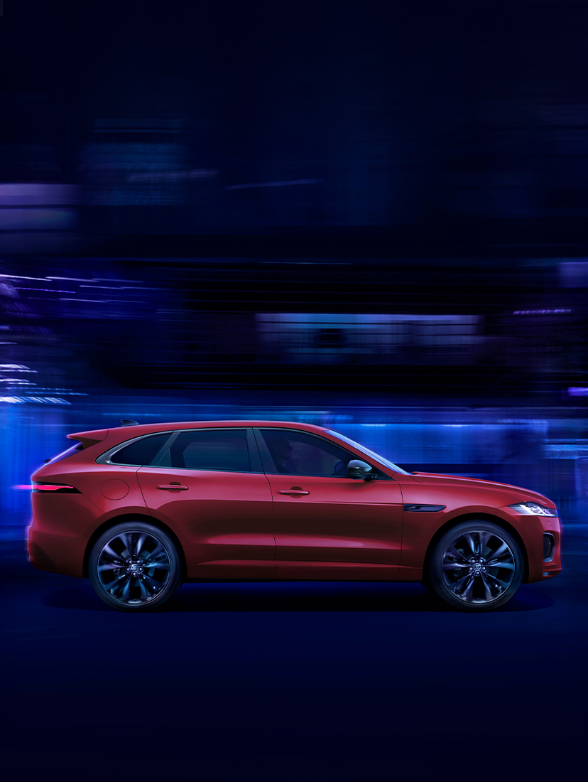 Red Jaguar F-PACE SUV driving at night through a tunnel with blue lights, showcasing its sleek performance and luxury design.