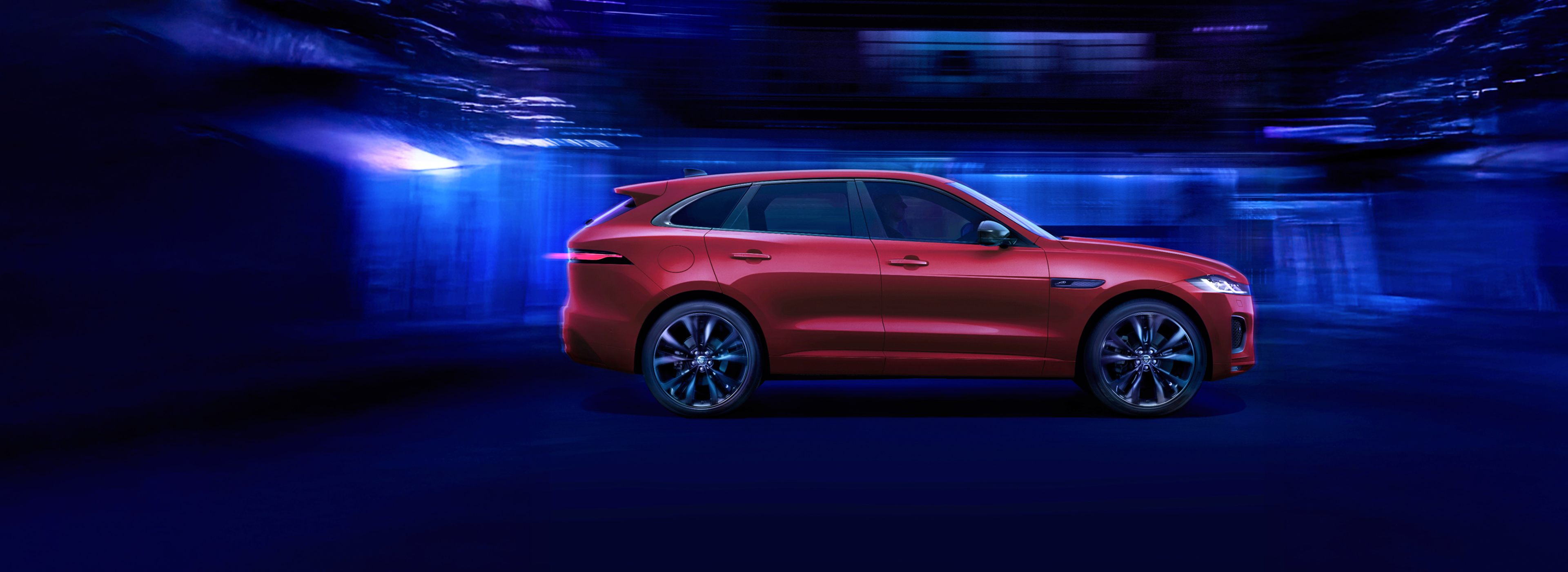 Red Jaguar F-PACE SUV driving at night through a tunnel with blue lights, showcasing its sleek performance and luxury design.