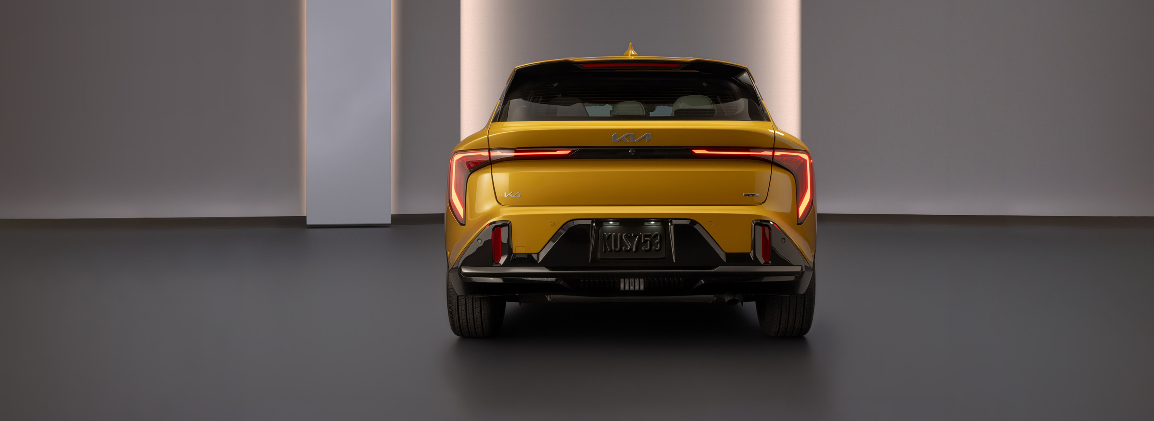Rear view of a yellow Kia K4 sedan with illuminated LED taillights in a modern studio setting.